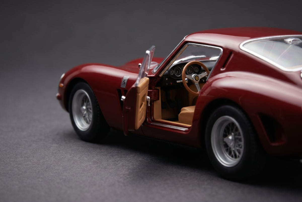 Macro close-up of a die-cast 1:18 scale model sports car with its driver door open, showing the cast metal body, detailed cabin and brushed-aluminium wheels